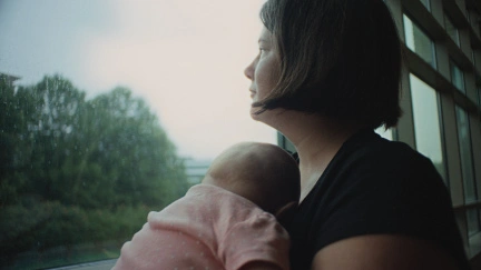 mother holding sleeping child closely, looking out window